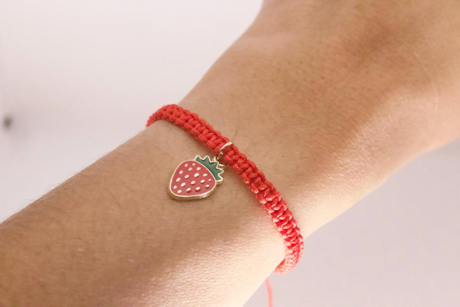 Adjustable friendship bracelet with strawberry charm worn on wrist