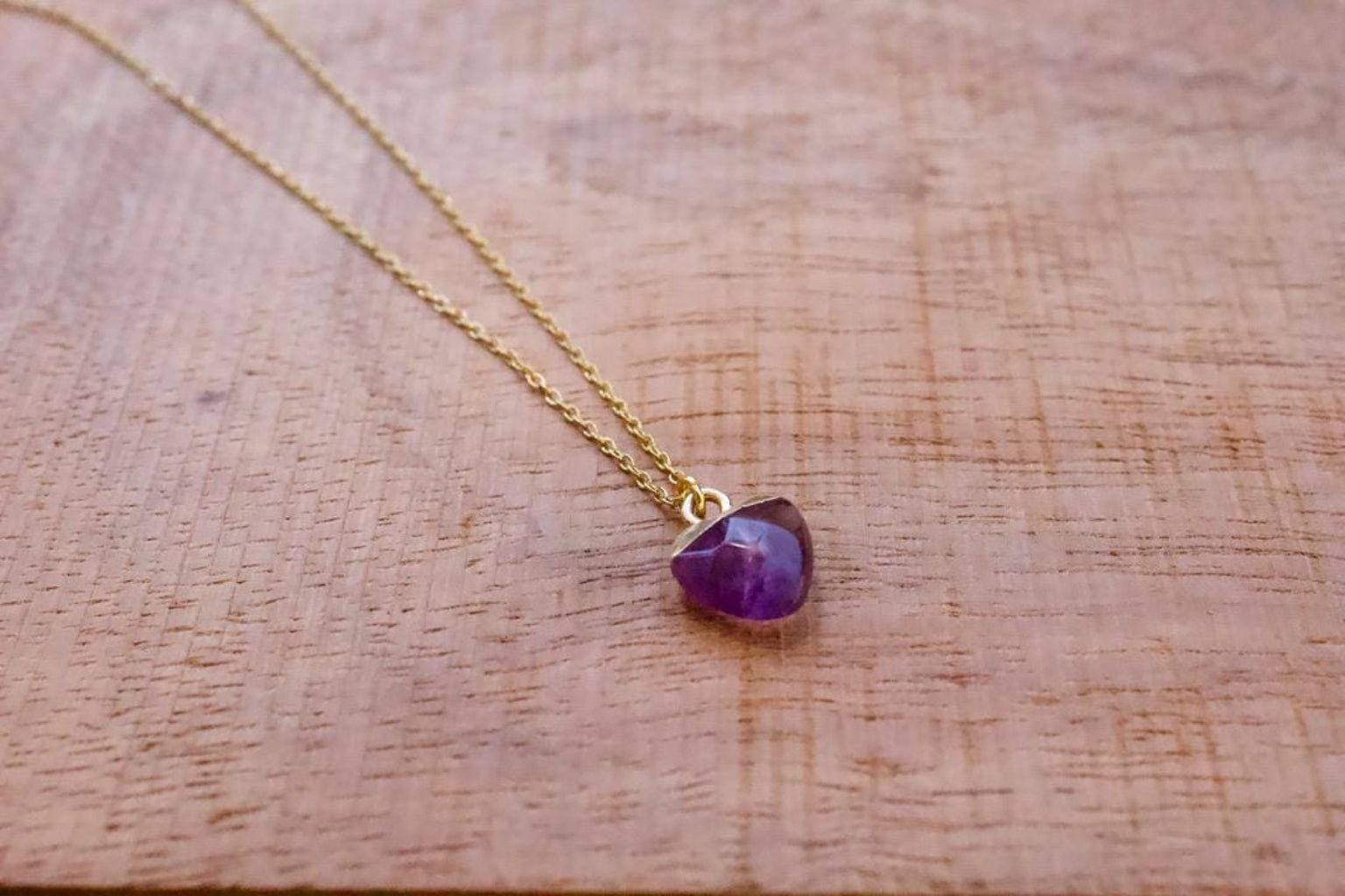 Gold necklace with a purple gemstone pendant on a wooden surface