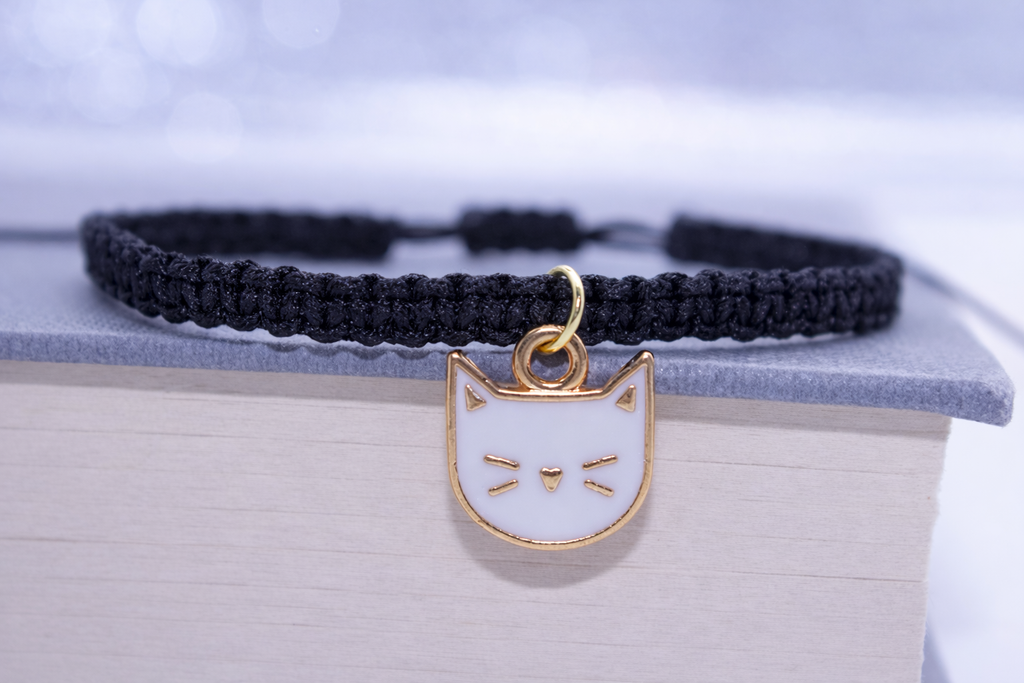 Black bracelet with a gold cat-shaped pendant on a white surface