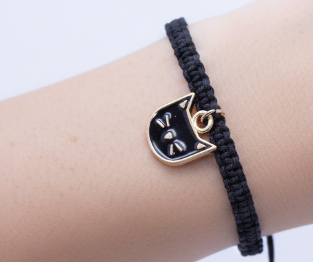 Black braided bracelet with a gold and black cat charm on a wrist against a white background