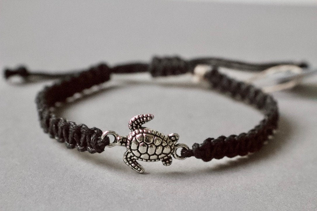 Black braided bracelet with a silver turtle charm on a light gray background