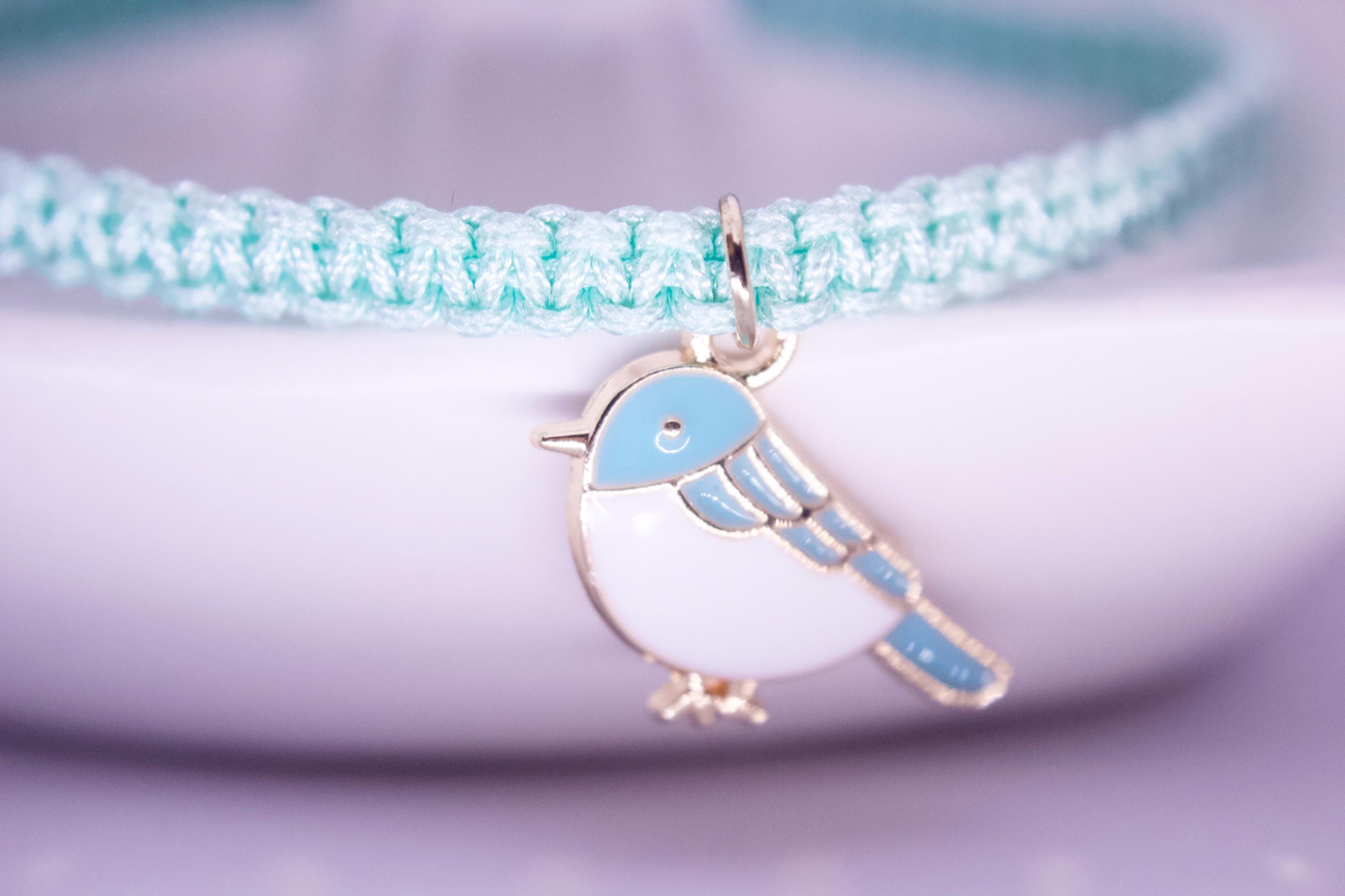 Bracelet with a blue bird charm on a light blue cord against a white background