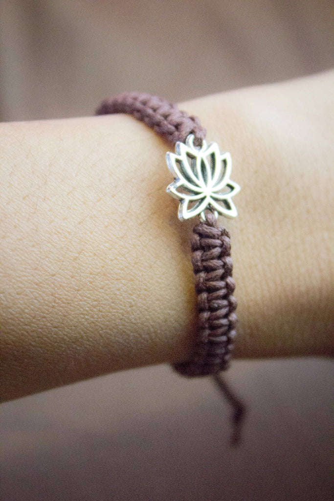 Bracelet with a silver lotus flower charm on a wrist against a neutral background