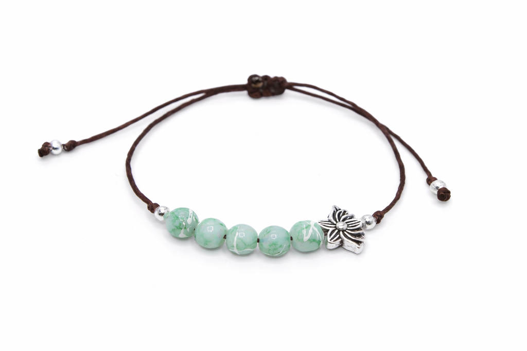 Bracelet with green swirl beads and a silver lotus charm on a white background