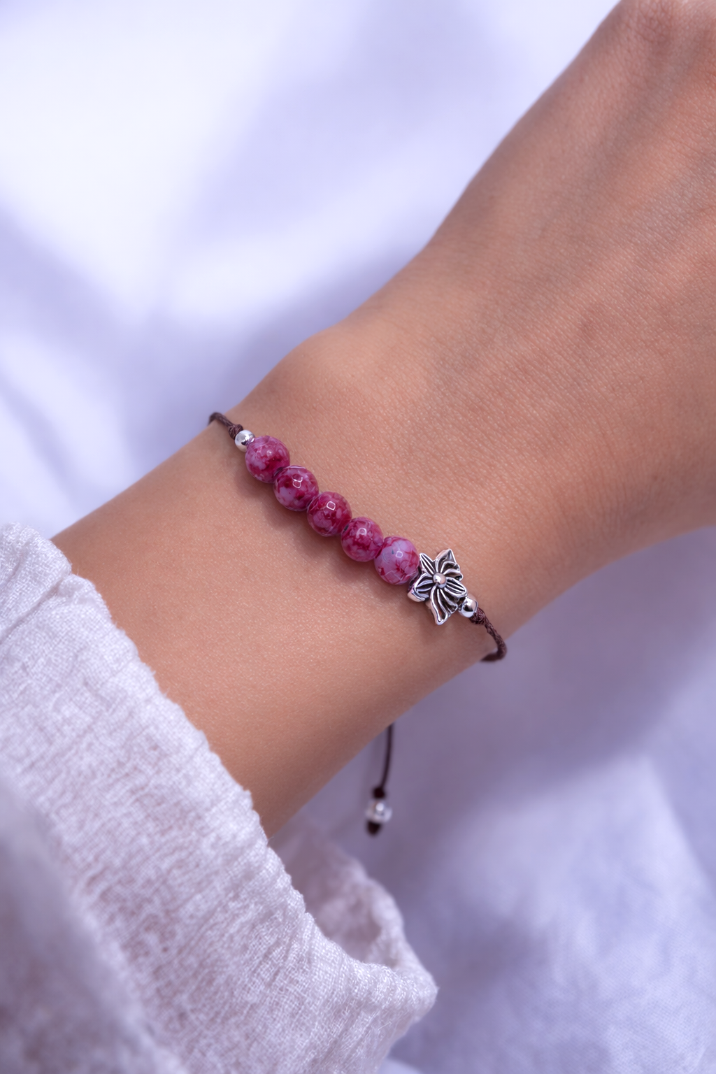 Bracelet with red beads and a lotus charm on a wrist