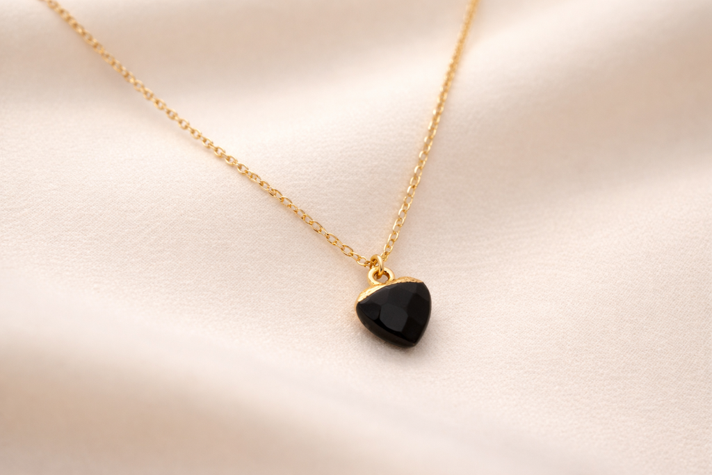 Gold necklace with a black pendant on a light pink background