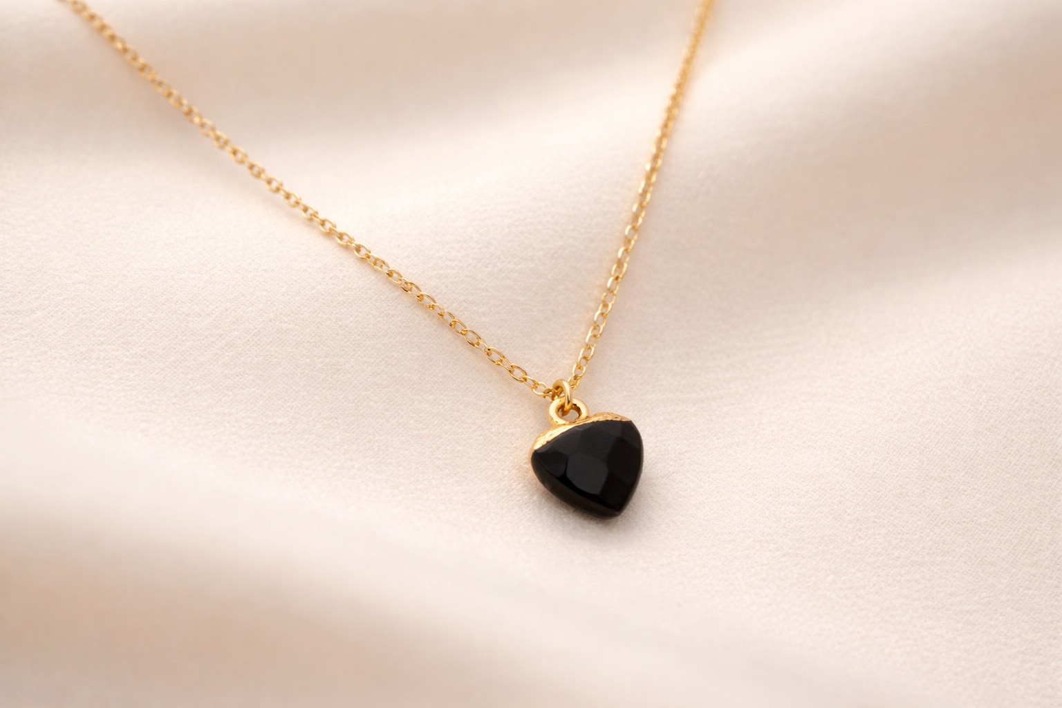 Gold necklace with a black pendant on a light pink background