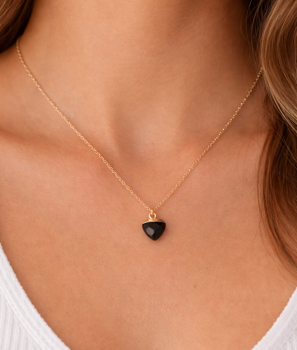 Gold necklace with a black heart pendant on a person wearing a white top.