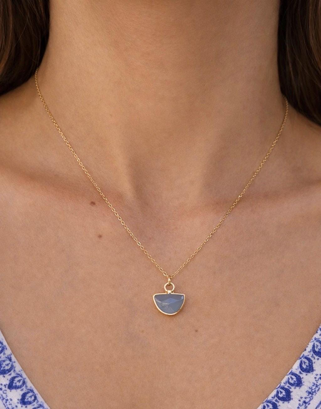 Gold necklace with a blue pendant worn by a person