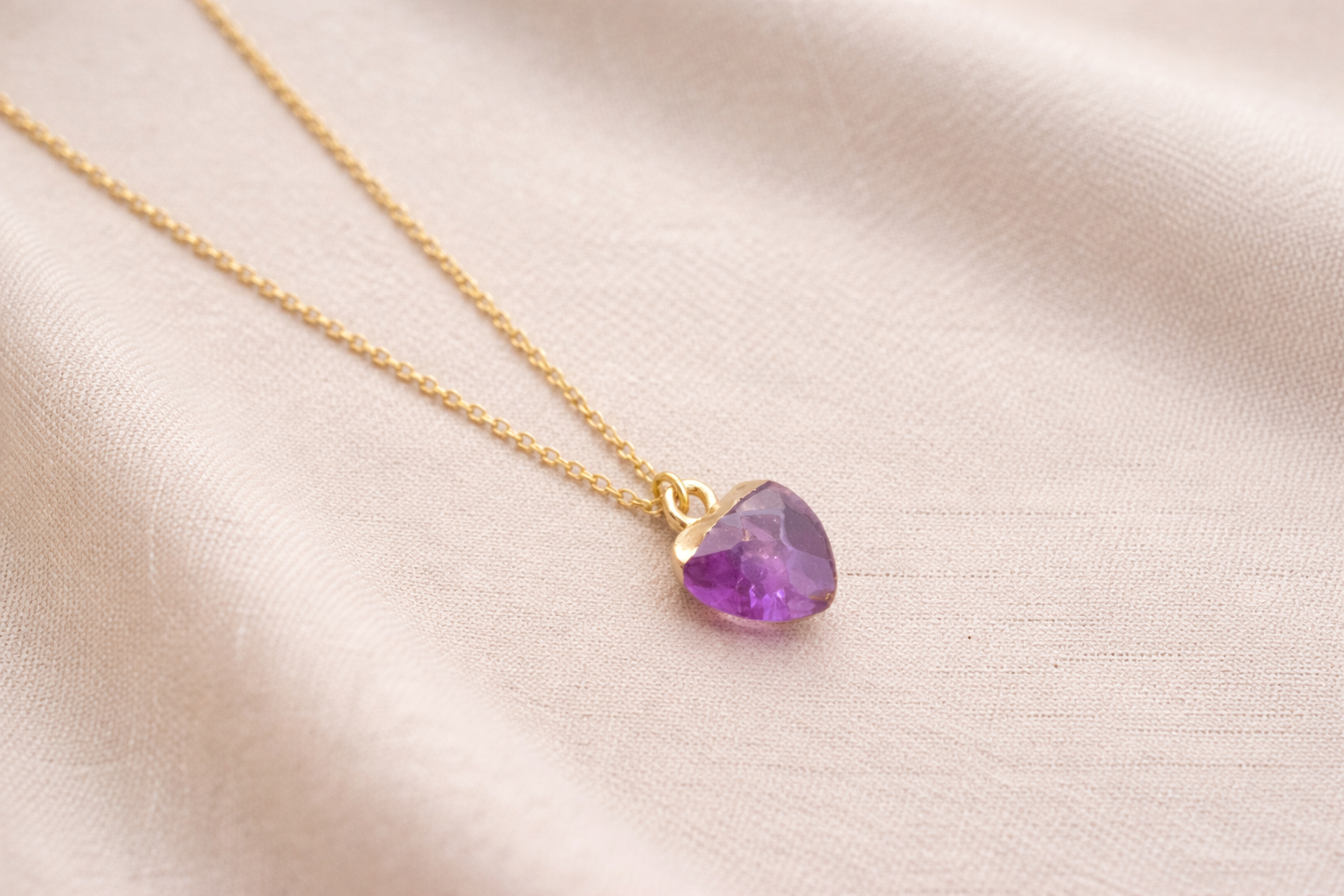 Gold necklace with a purple gemstone pendant on a light pink fabric background