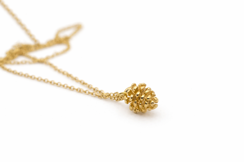 Gold pinecone charm necklace on white background, delicate nature jewelry gift