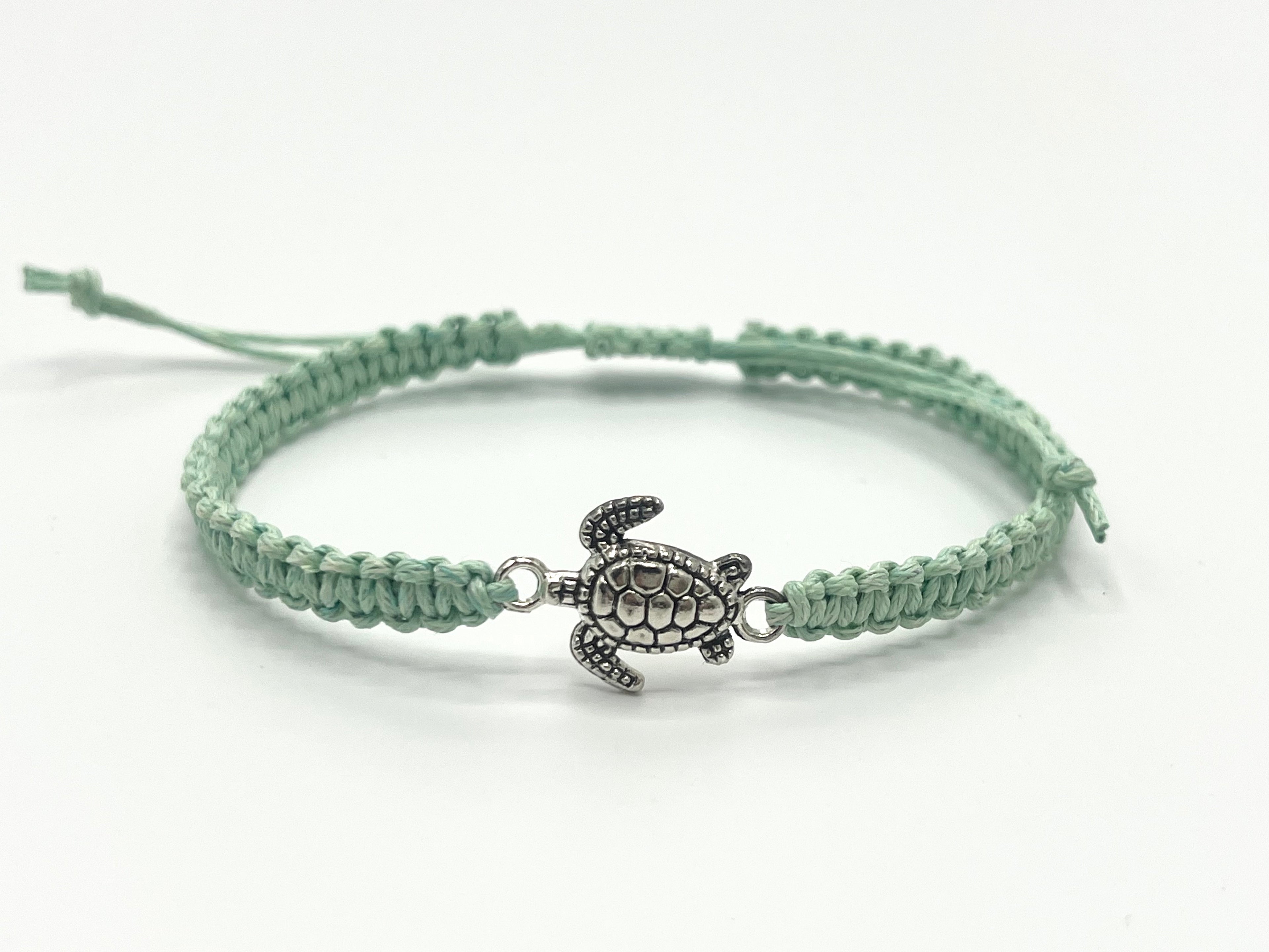 Green braided bracelet with a turtle charm on a white background