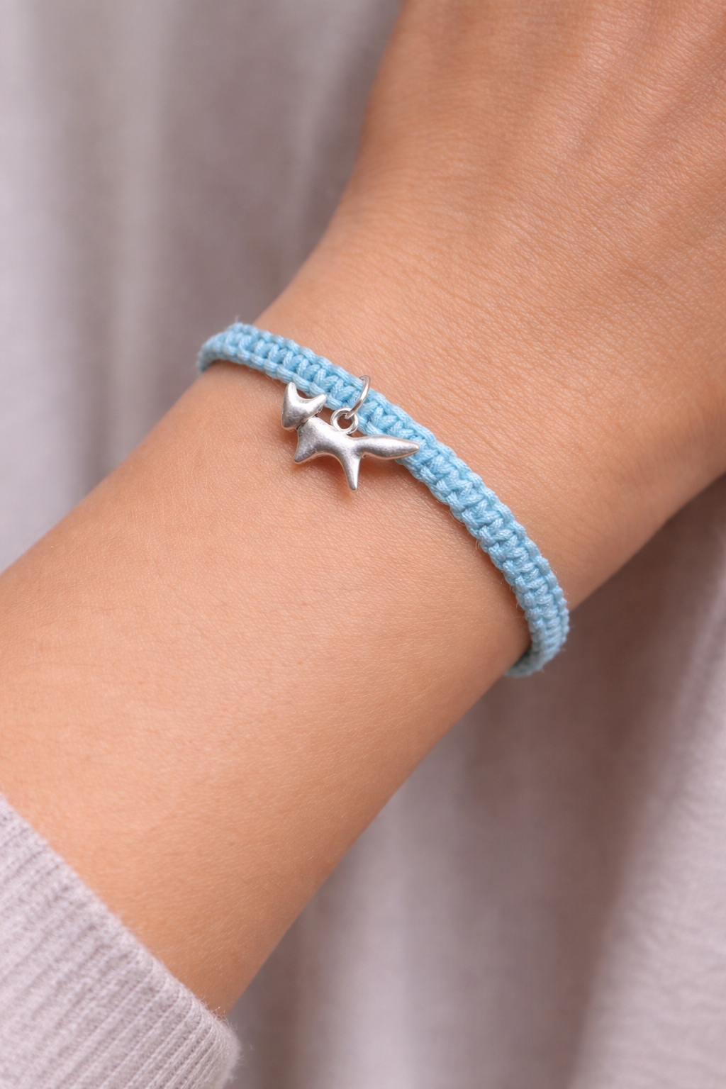 Light blue bracelet with a fox charm on a wrist against a neutral background