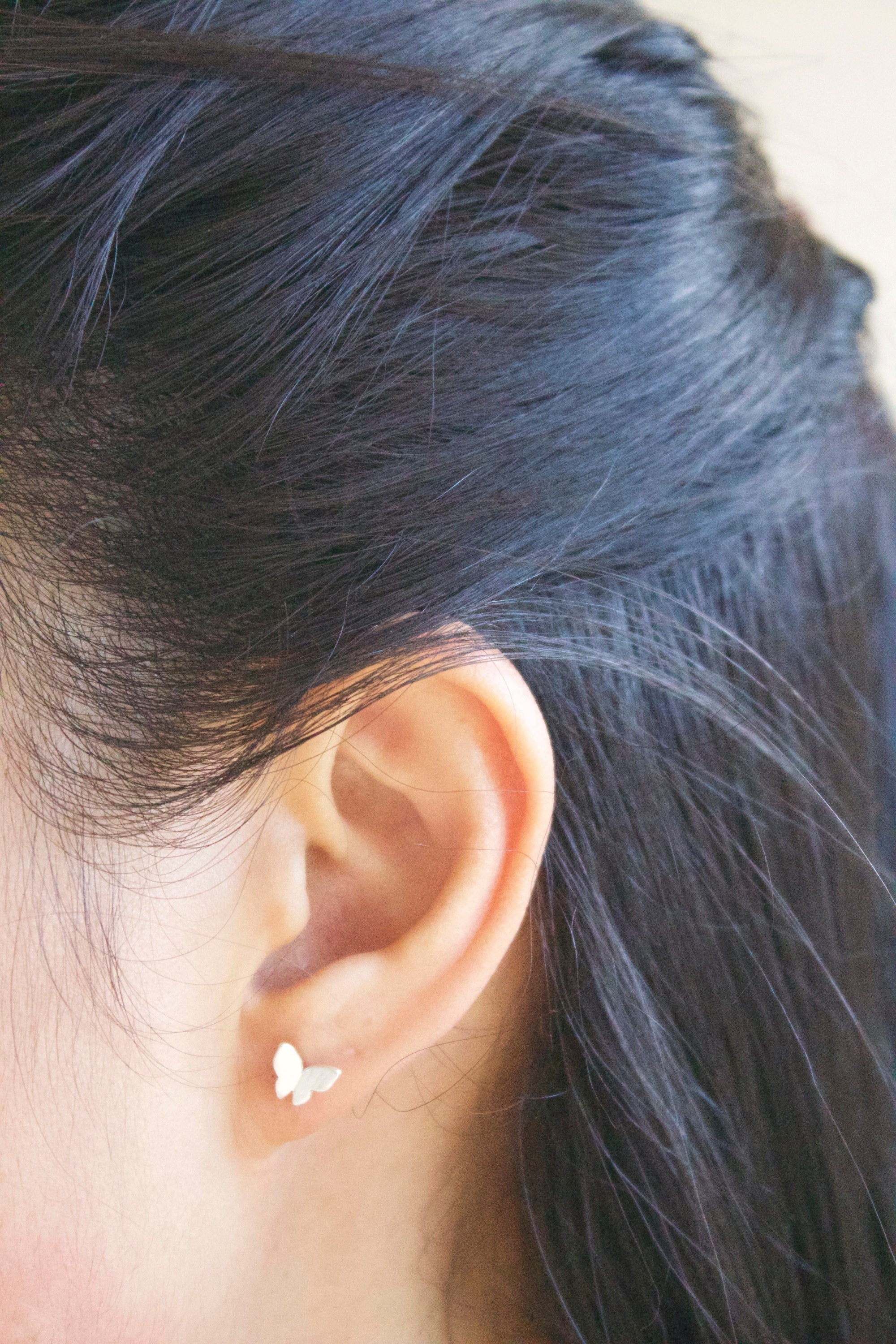 Minimalist sterling silver butterfly stud earrings worn by woman