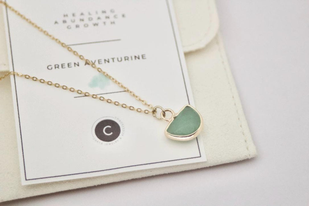 Gold necklace with a green pendant on a card with product details.