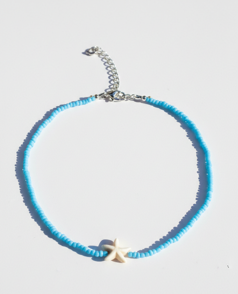Blue beaded necklace with a starfish charm on a light gray background