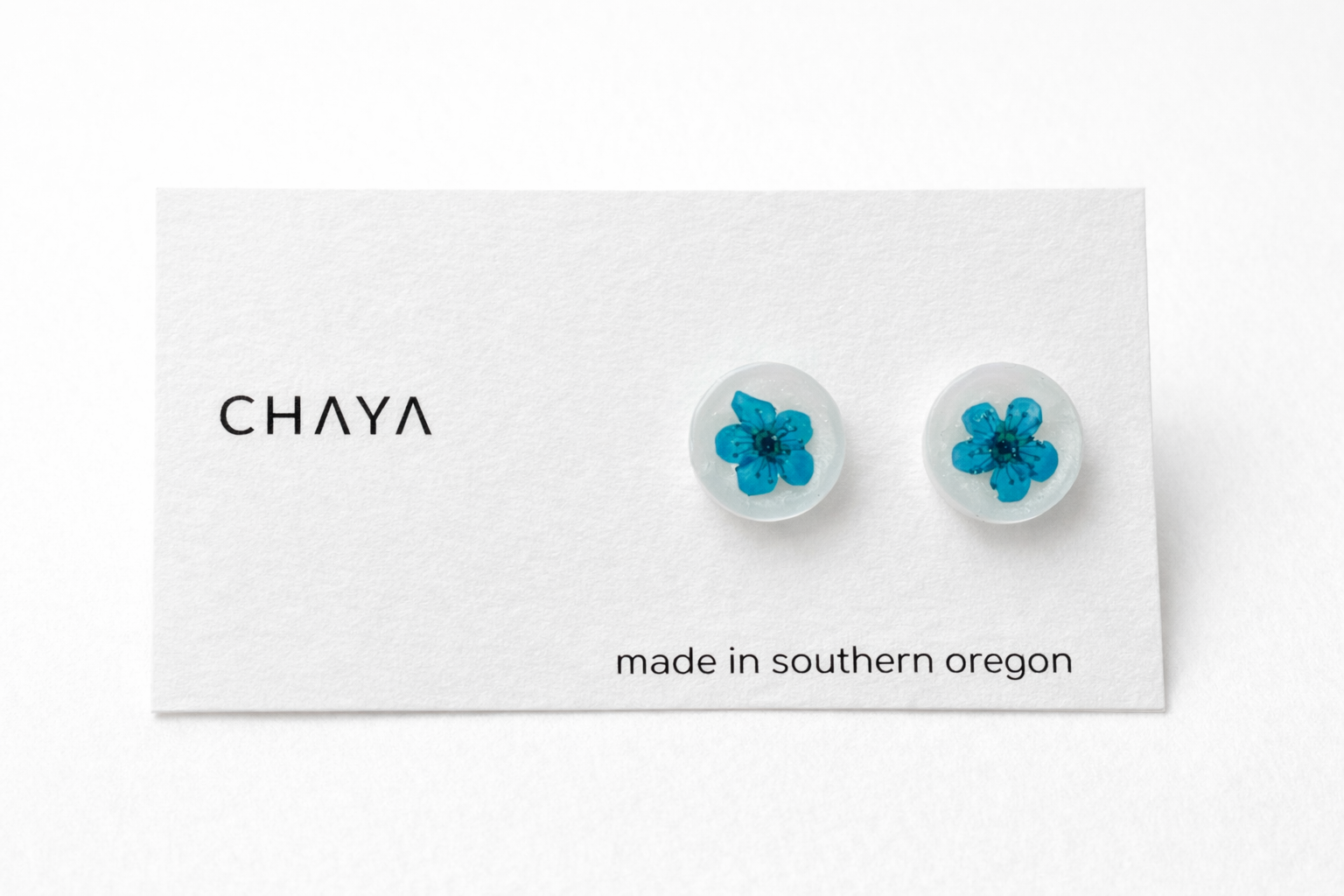 Pair of earrings with blue flowers on a Chaya branded card.