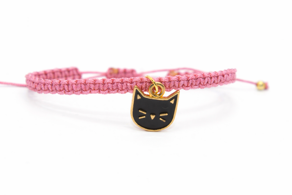 Pink braided bracelet with a black cat charm on a white background
