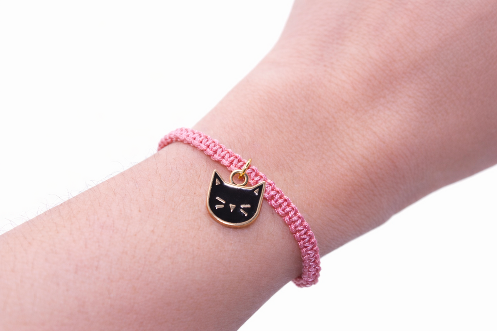 Pink bracelet with a cat charm on a wrist against a white background