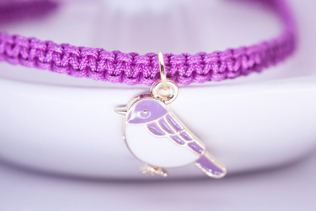 Purple braided bracelet with a bird charm on a light purple background
