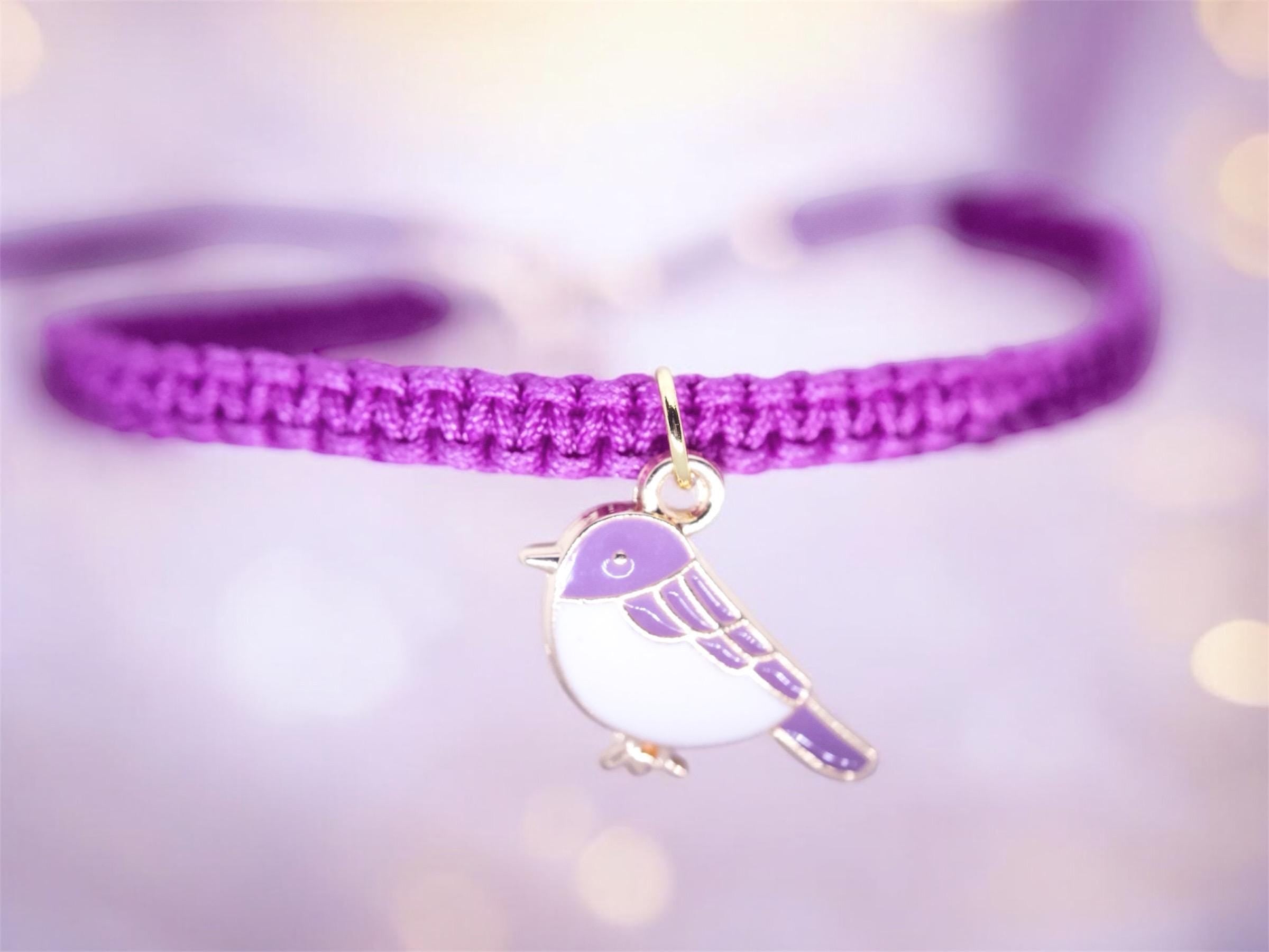 Purple braided bracelet with a bird charm on a blurred light background