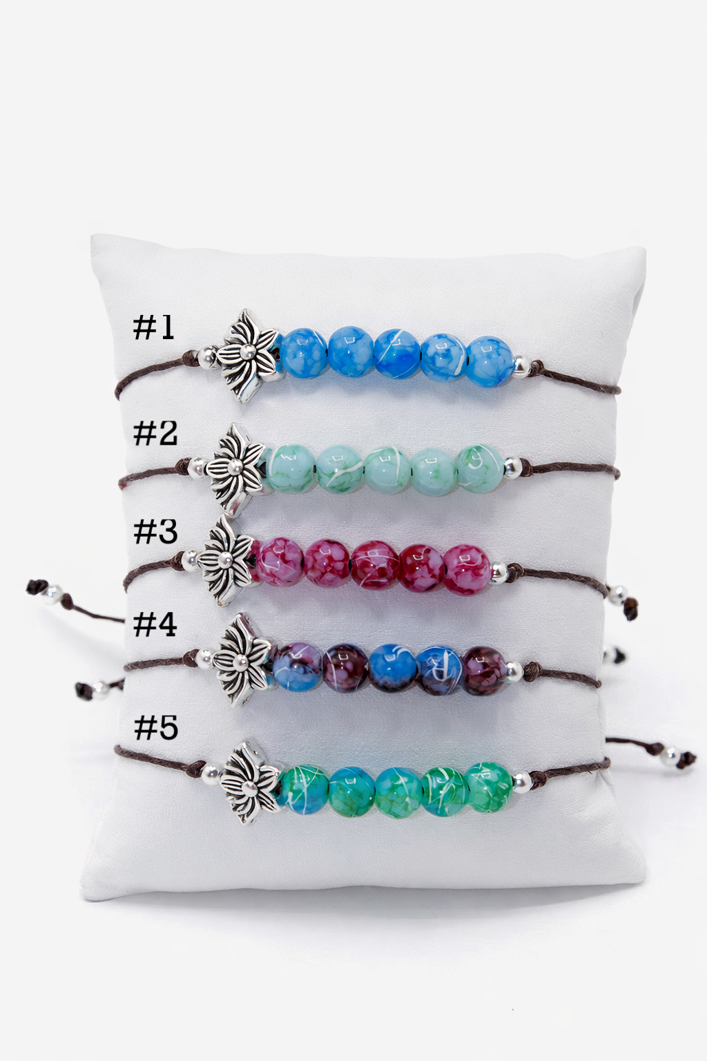 Set of five beaded bracelets with lotus charms on a white cushion