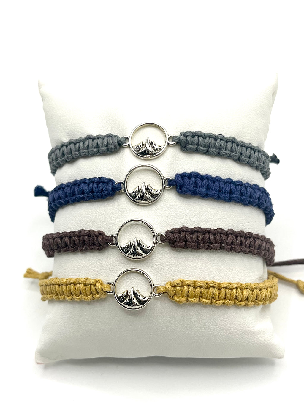 Set of four bracelets in gray, blue, brown, and beige on a white stand.