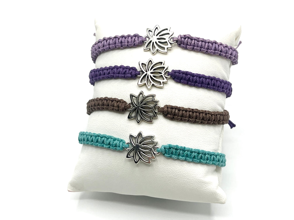 Set of four macrame bracelets with lotus flower charms on a white pillow.