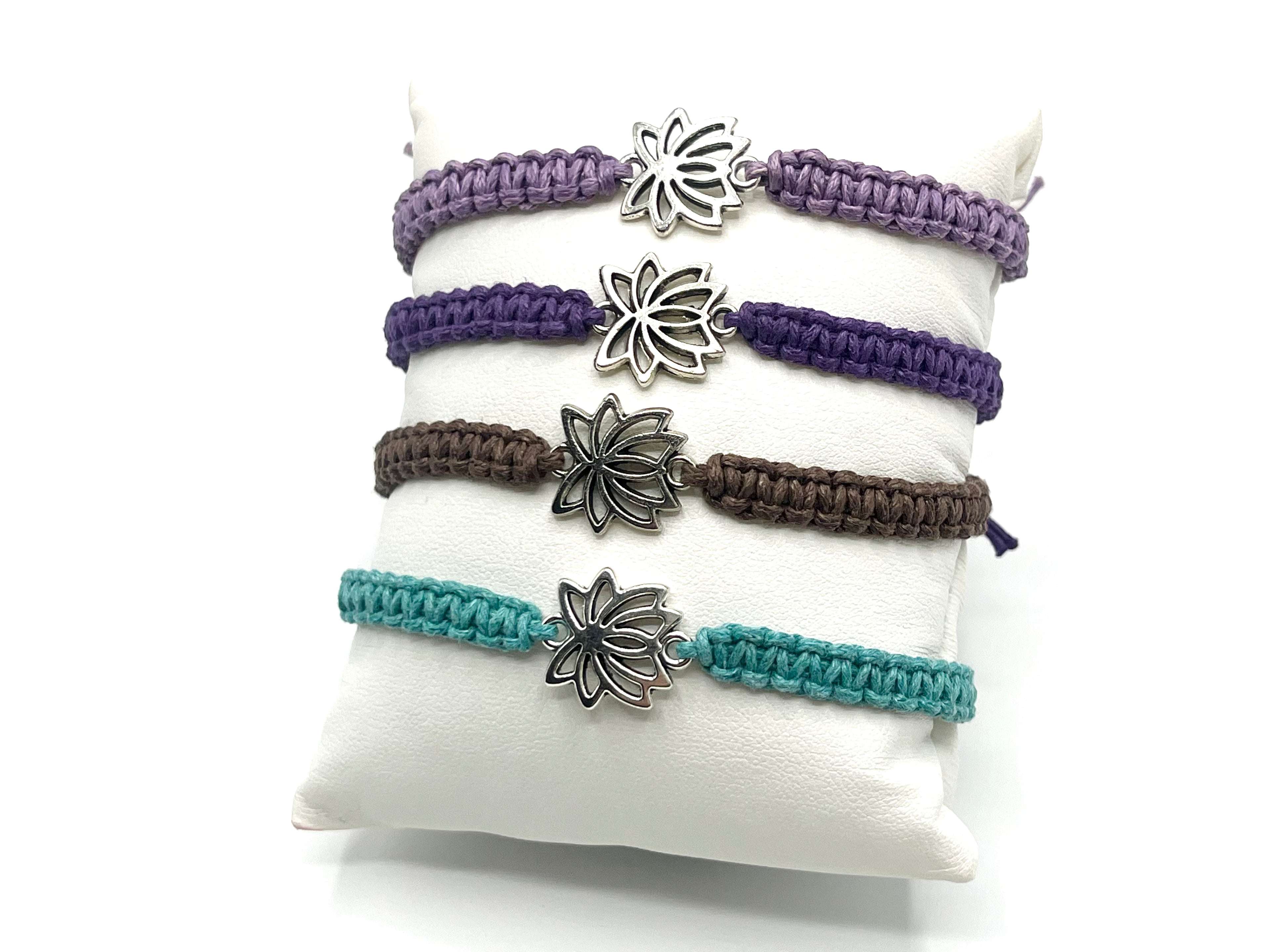 Set of four macrame bracelets with lotus flower charms on a white pillow.