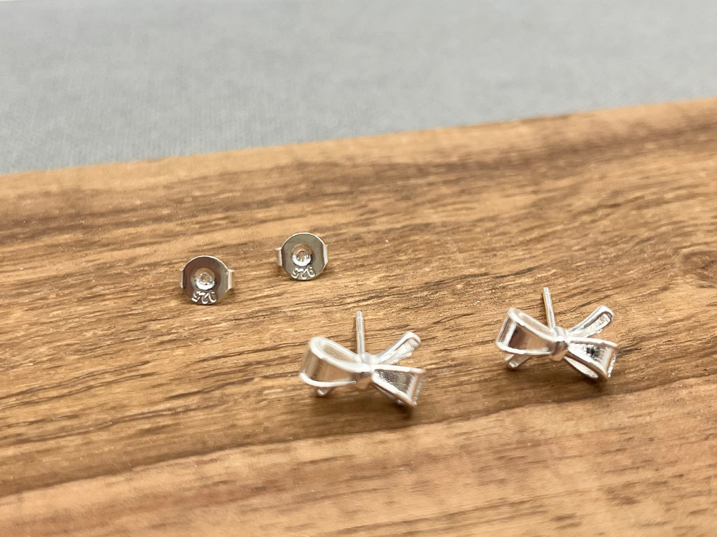 Set of silver bow-shaped earrings on a wooden surface