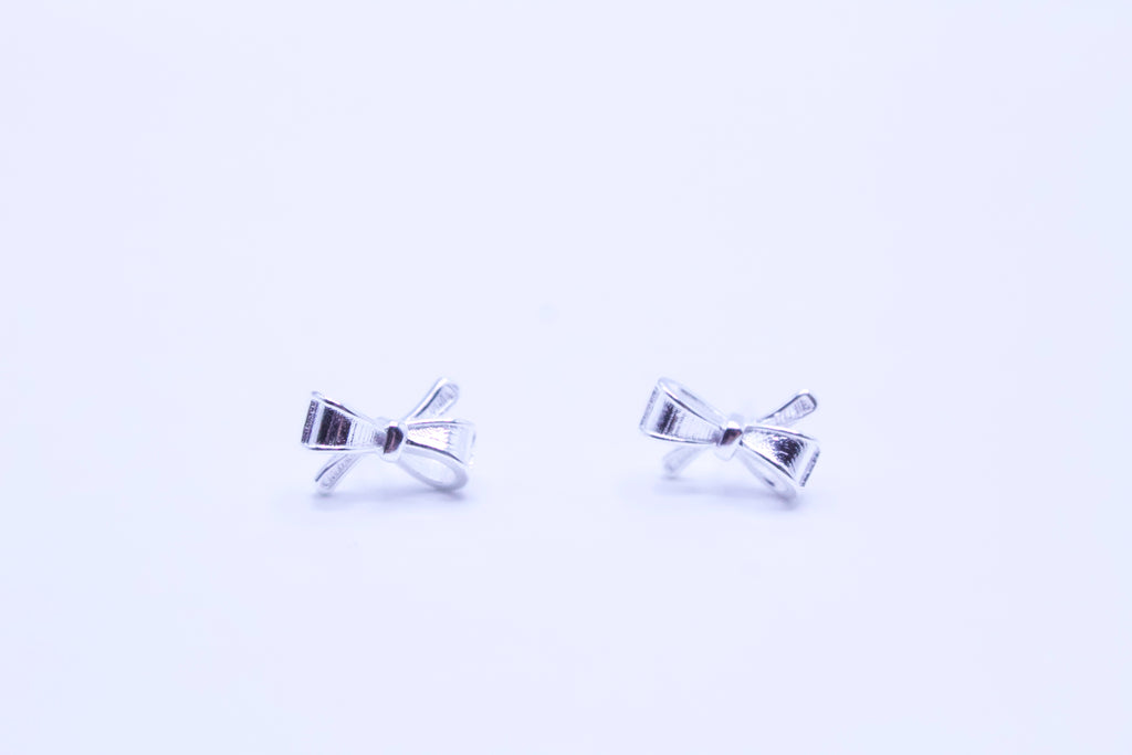 Silver bow-shaped earrings on a light purple background