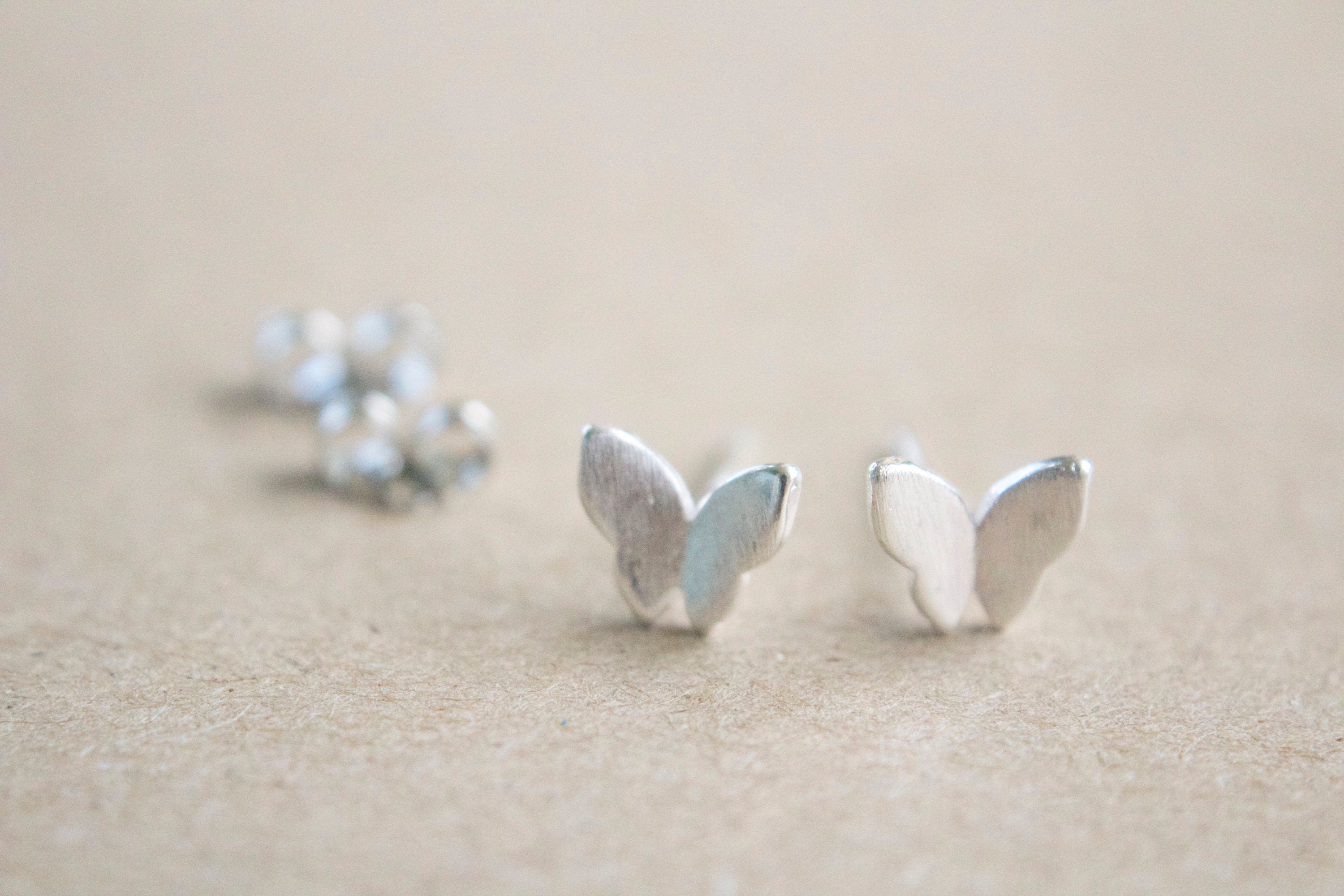 Silver butterfly earrings on a beige surface