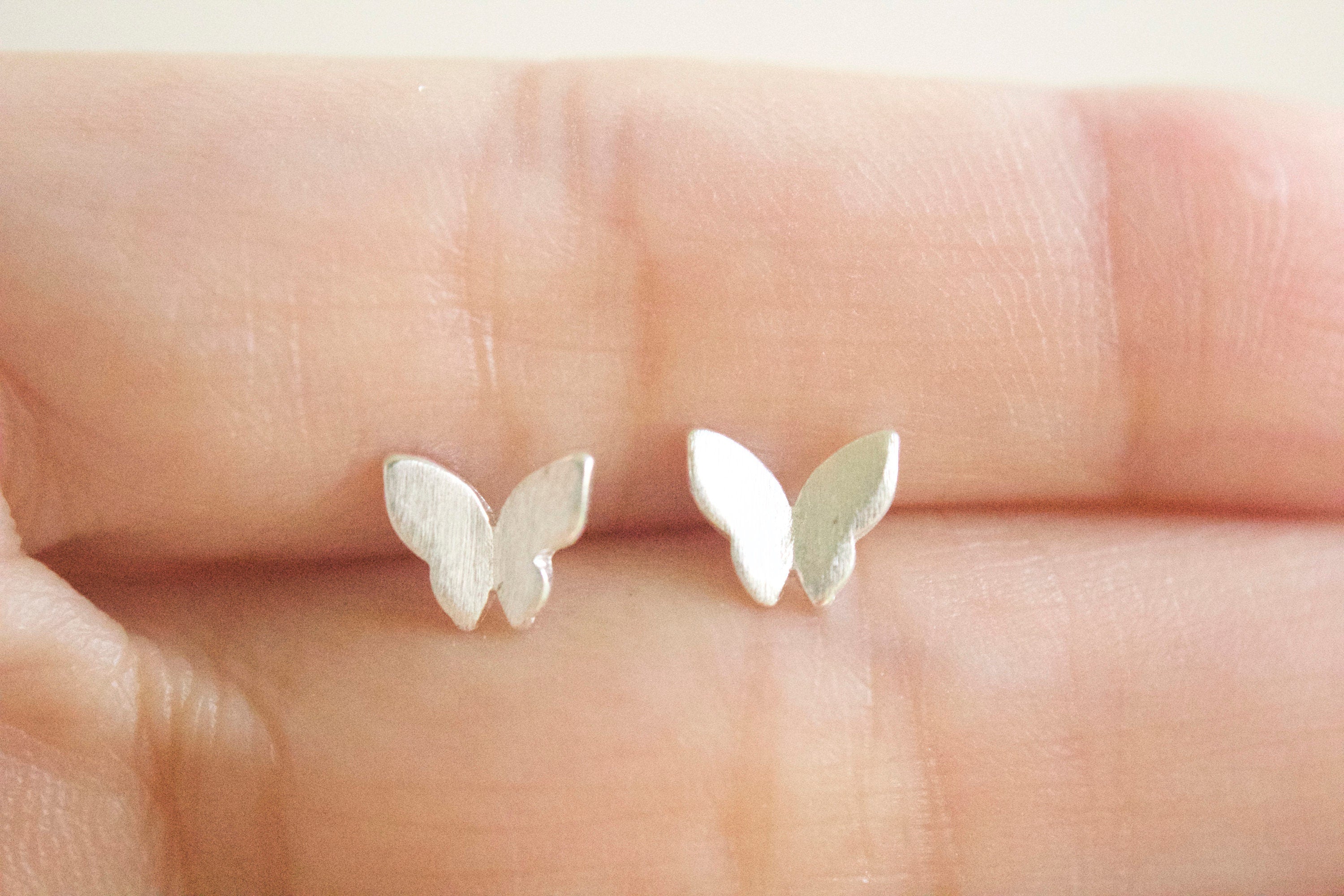 Silver butterfly earrings held between fingers on a light skin background