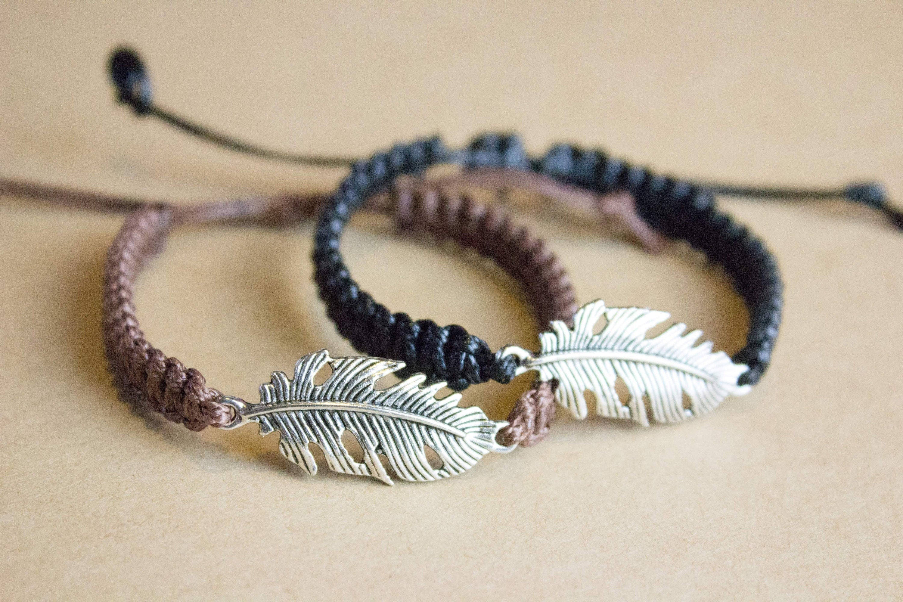 Two braided bracelets with feather charms on a beige background