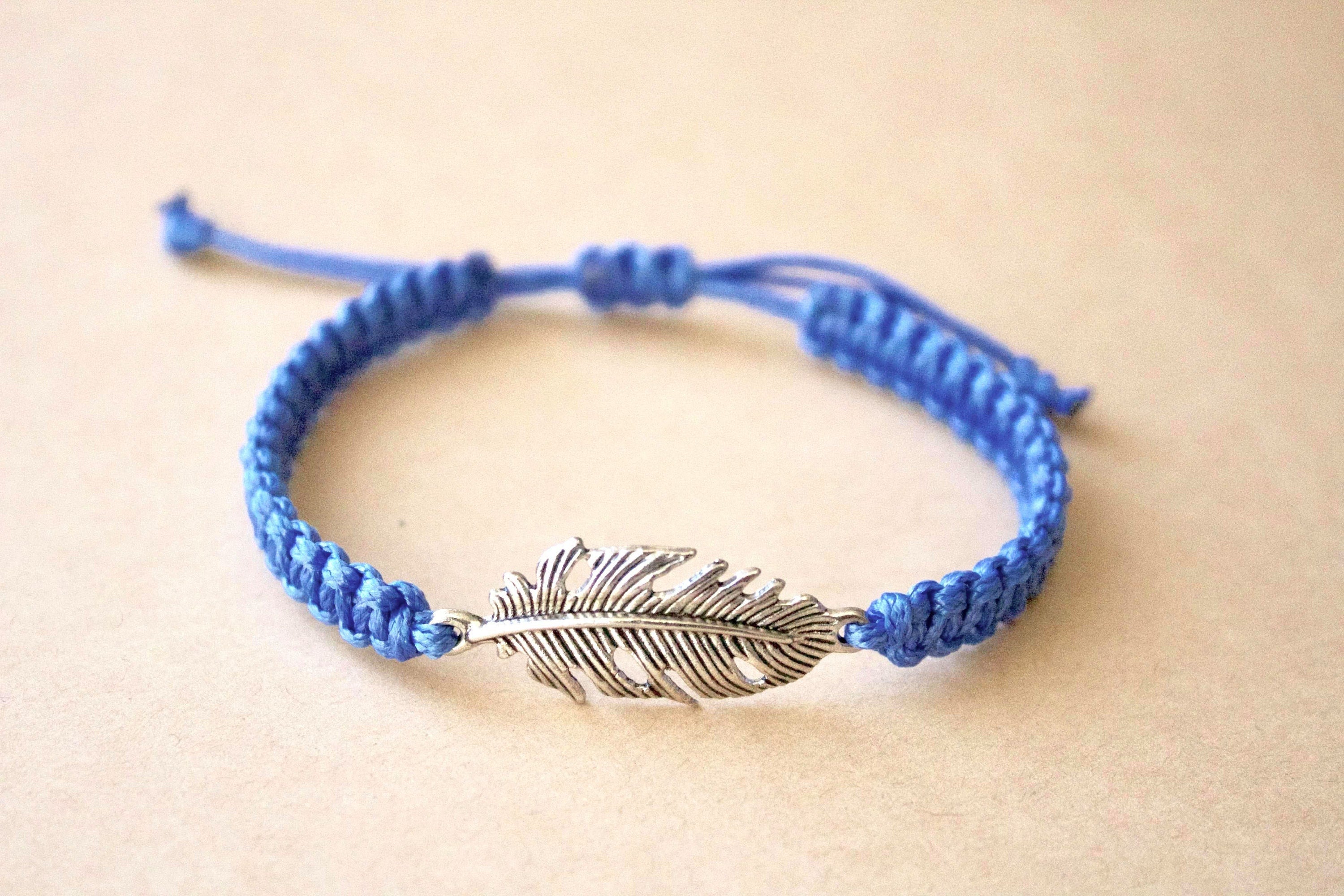Blue braided bracelet with a silver feather charm on a beige background
