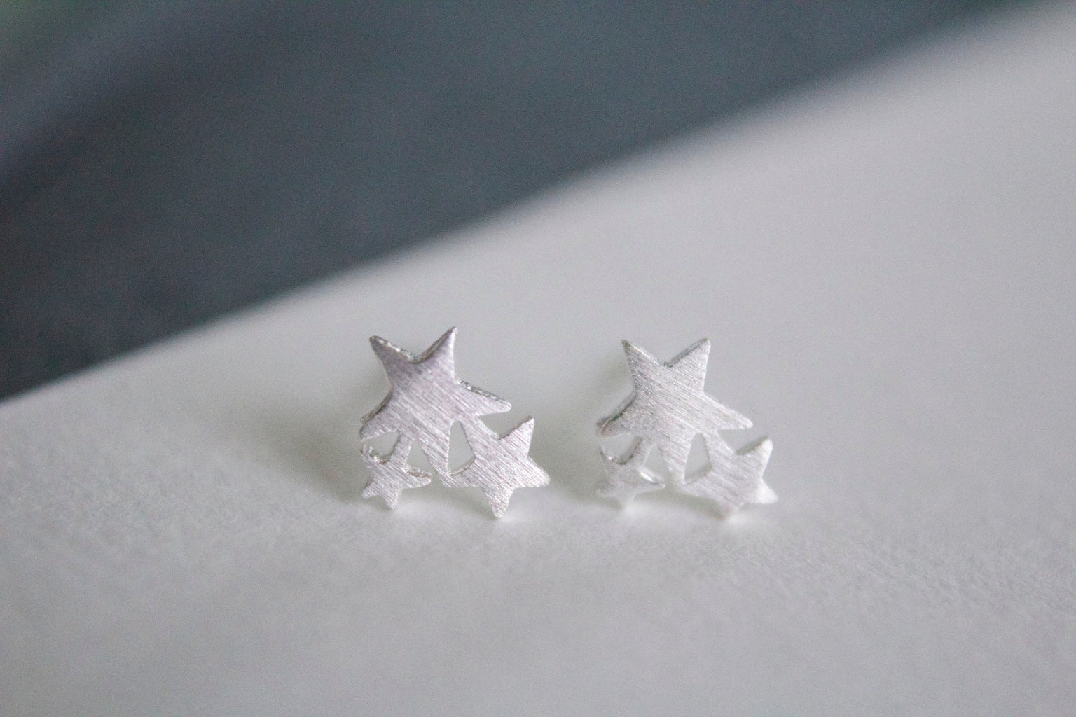 Silver star-shaped earrings on a light gray surface with a dark gray background