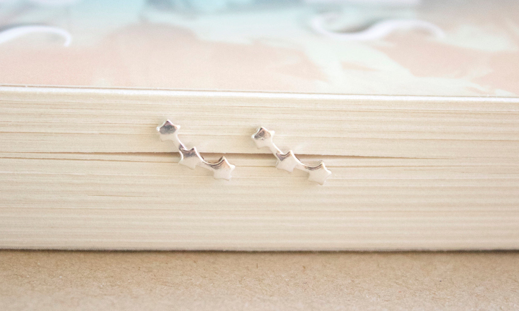Silver three star-shaped earrings on a beige surface