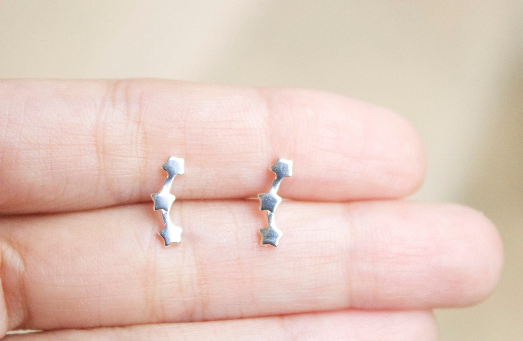 Silver star-shaped earrings held between fingers against a neutral background