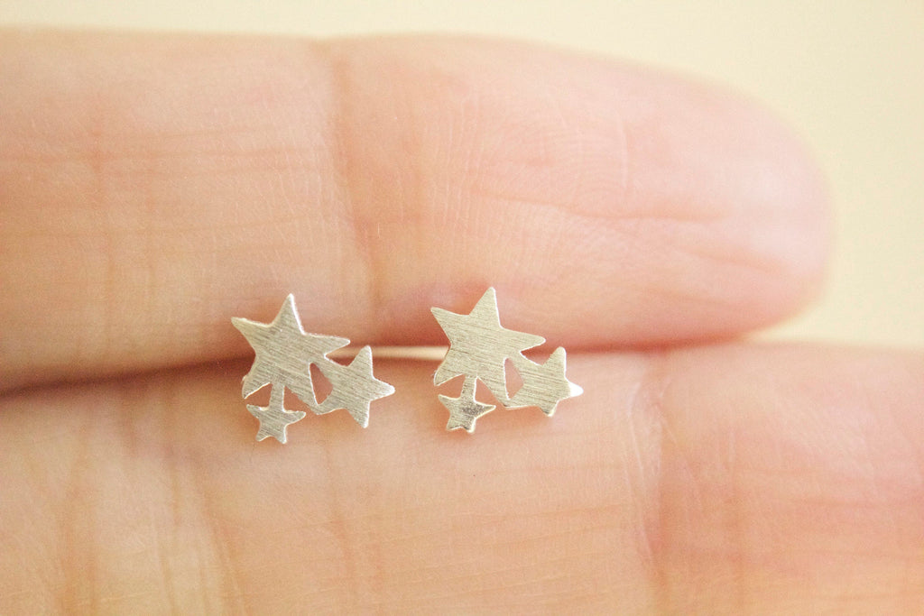 Star-shaped earrings held between fingers on a blurred background