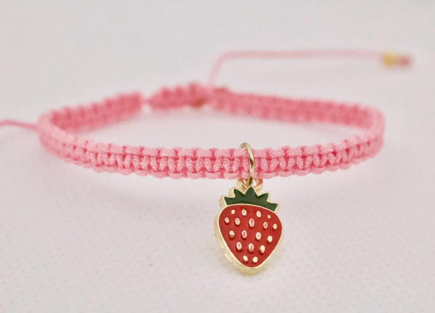Pink braided bracelet with a strawberry charm on a light pink background