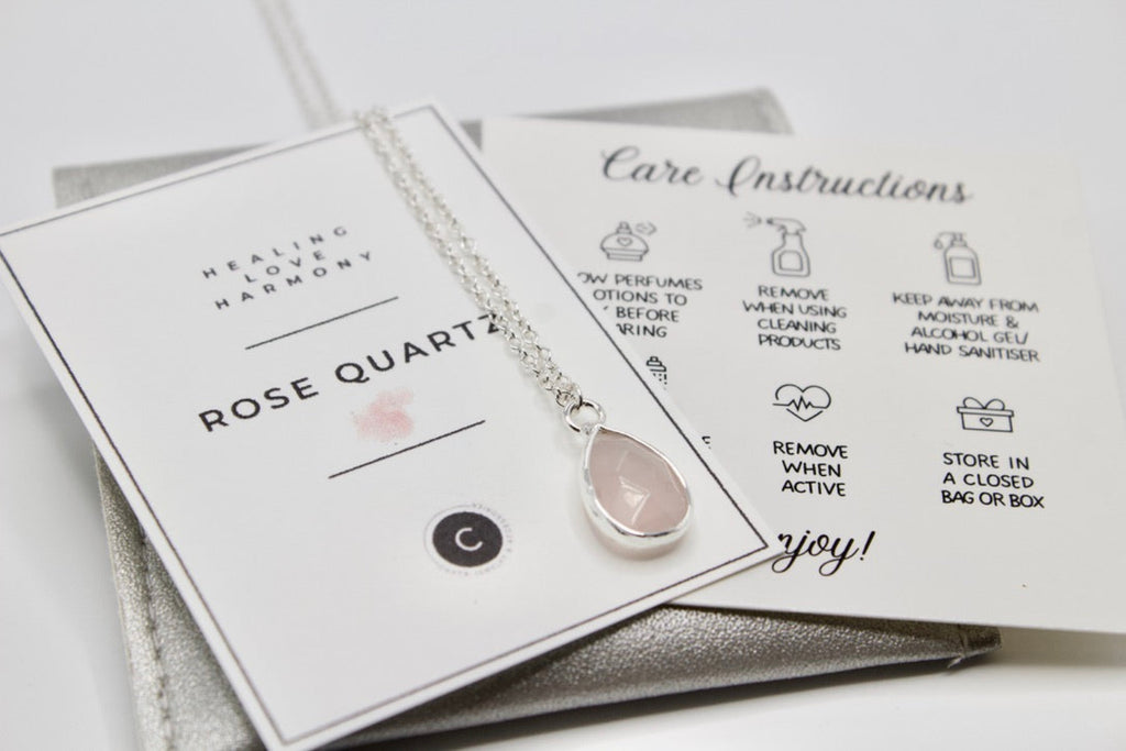 Necklace with rose quartz pendant on a branded card with care instructions.