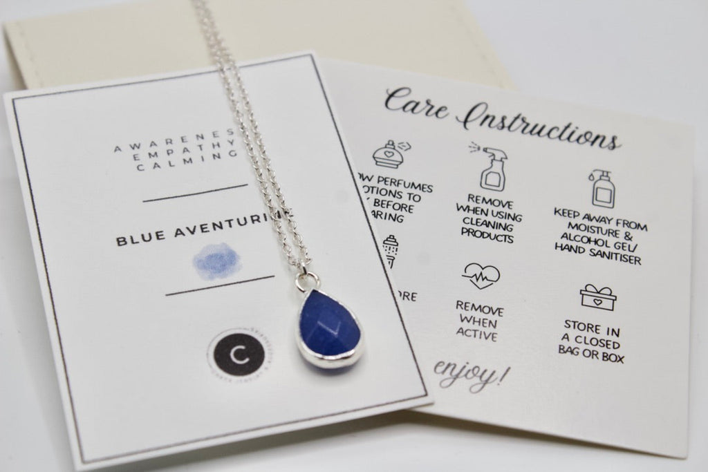 Blue teardrop pendant necklace on a card with care instructions