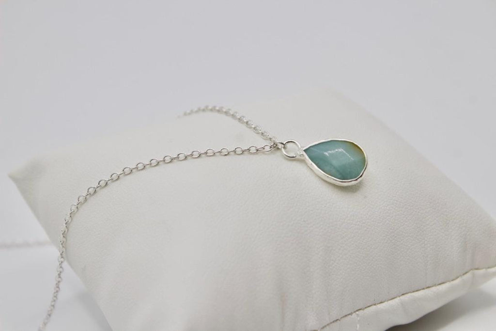 Silver bracelet with a green teardrop pendant on a white cushion
