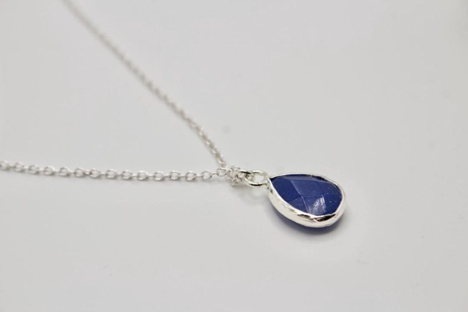 Teardrop-shaped blue pendant on a silver chain against a light gray background