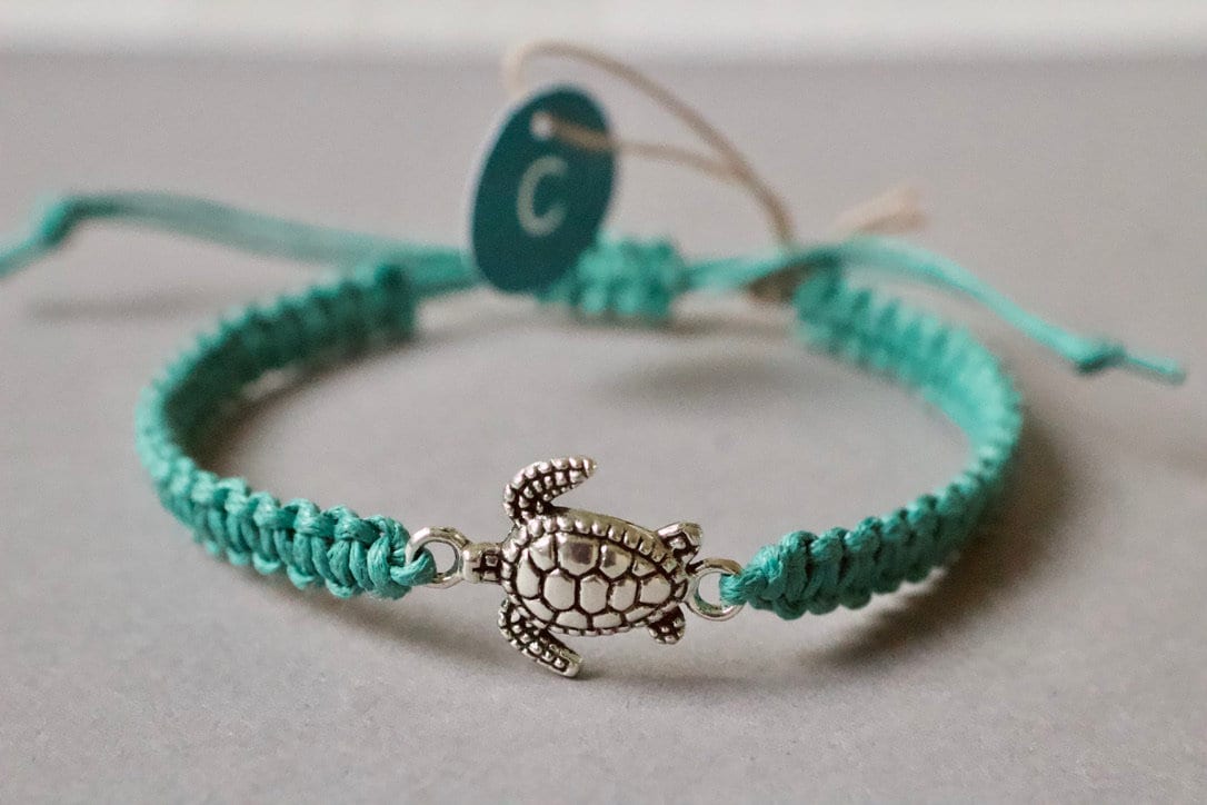 Turquoise braided bracelet with a turtle charm on a light gray background