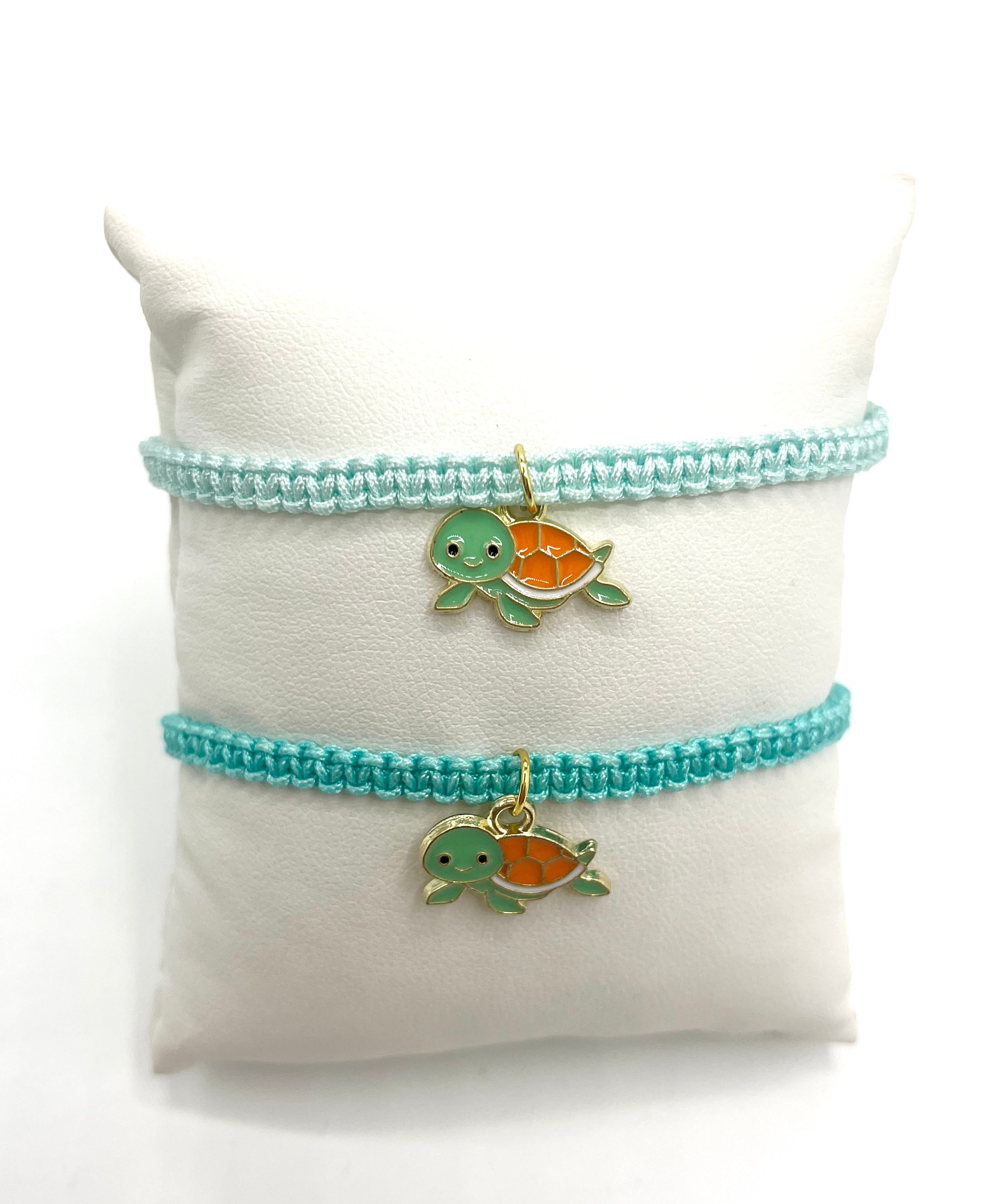 Two bracelets with turtle charms on a white cushion