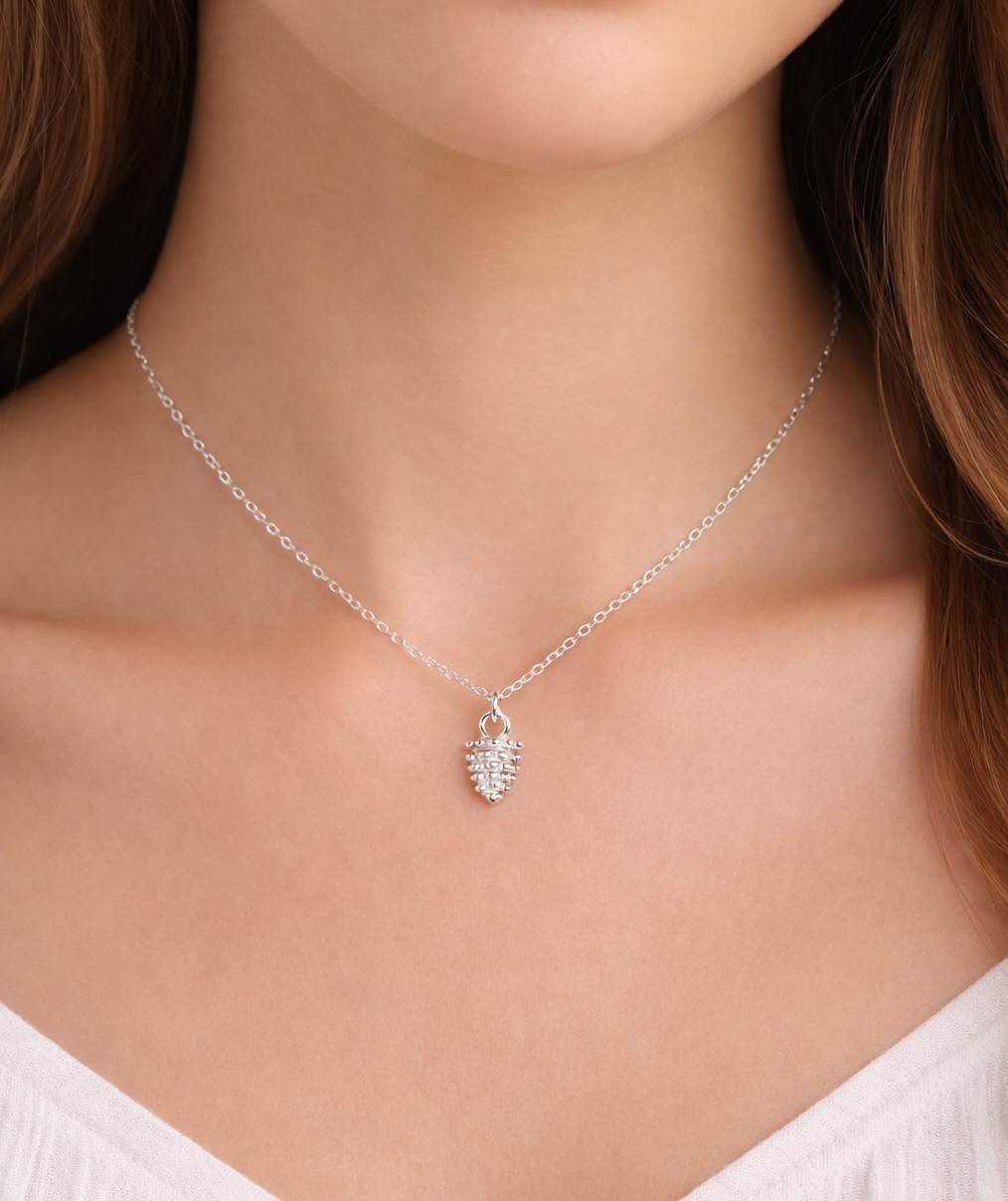 Woman wearing dainty pinecone charm necklace, layered minimalist forest jewelry look