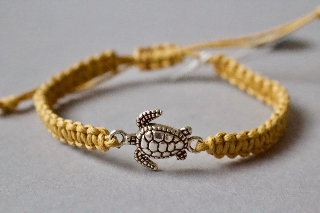 Yellow braided bracelet with a turtle charm on a gray background