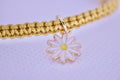 Gold bracelet with a daisy charm on a light purple background