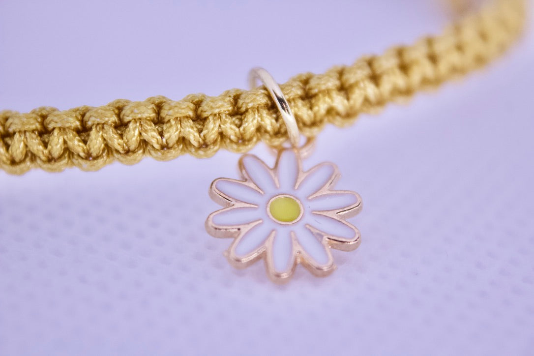 Gold bracelet with a daisy charm on a light purple background